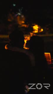 Two people sitting close together lit by firelight at night