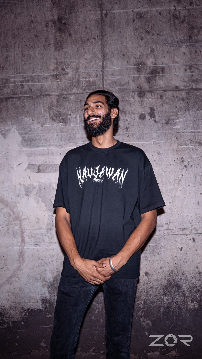 Man in an oversized black graphic tee laughing against a concrete wall