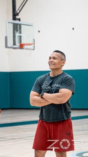 Coach smiling with arms crossed on an indoor basketball court
