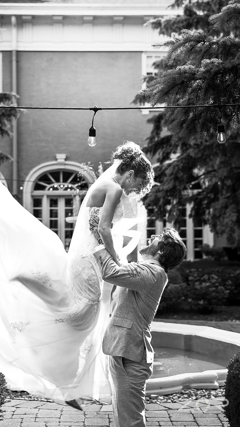 Groom lifting the bride off her feet beside a fountain, in black and white