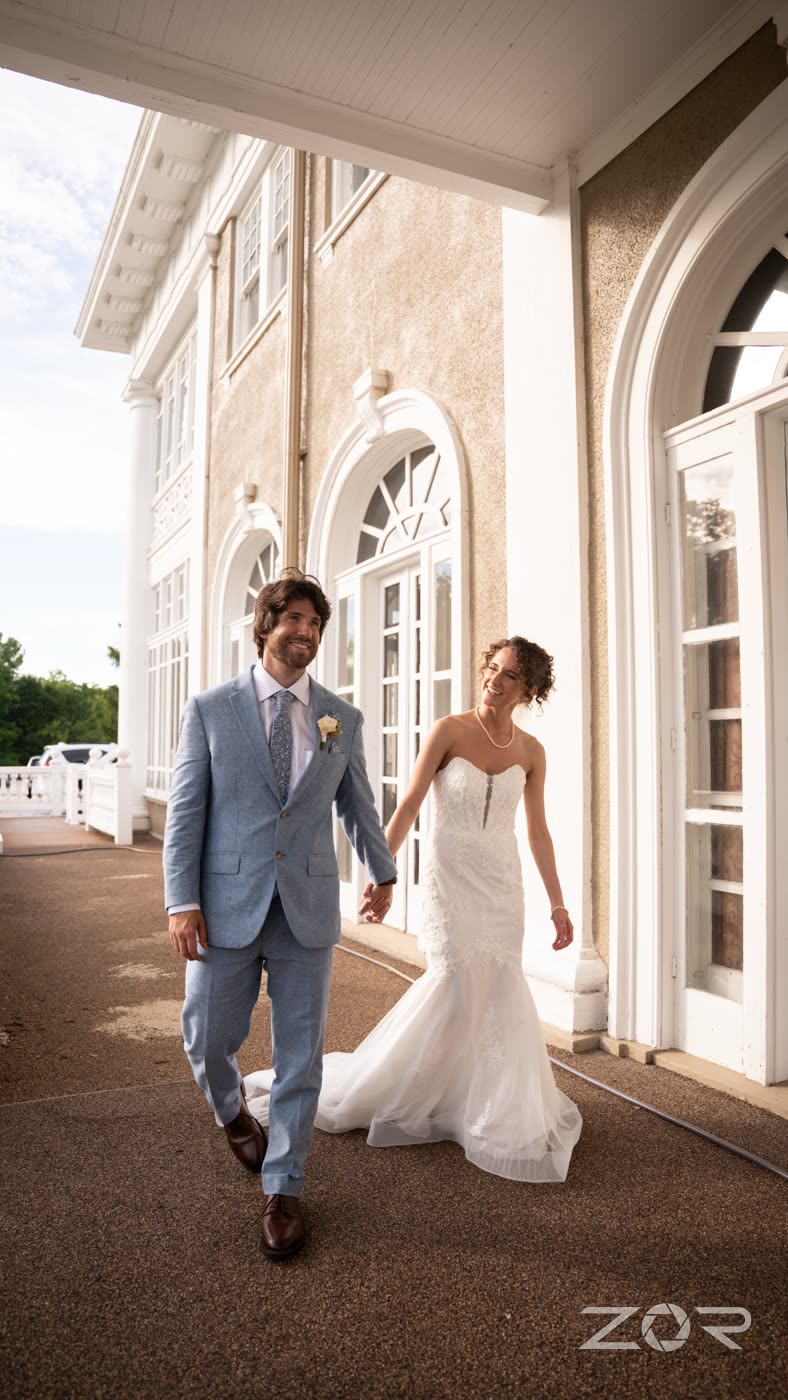 Bride and groom walking hand in hand along a mansion veranda
